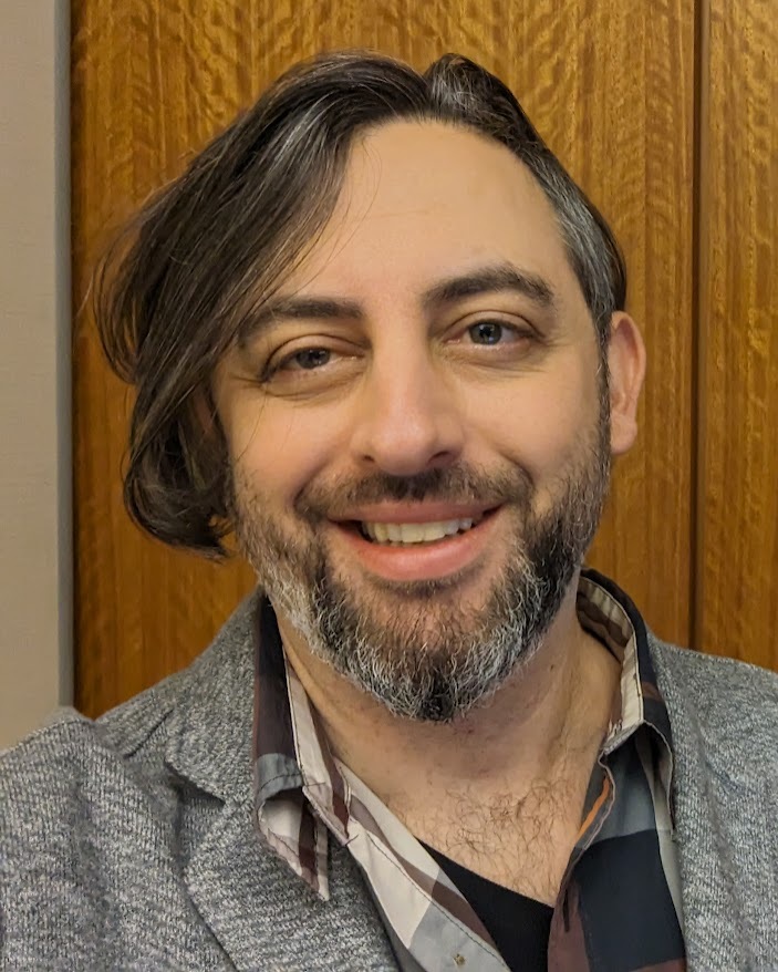 A selfie of Nick Reid (eg me). I'm a white guy with graying brown hair, a short beard, and hazel eyes.